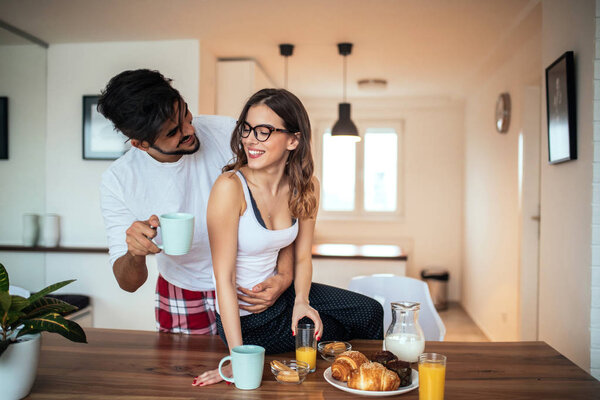 Photo of a young couple drinking coffee while having breakfast in the kitchen.