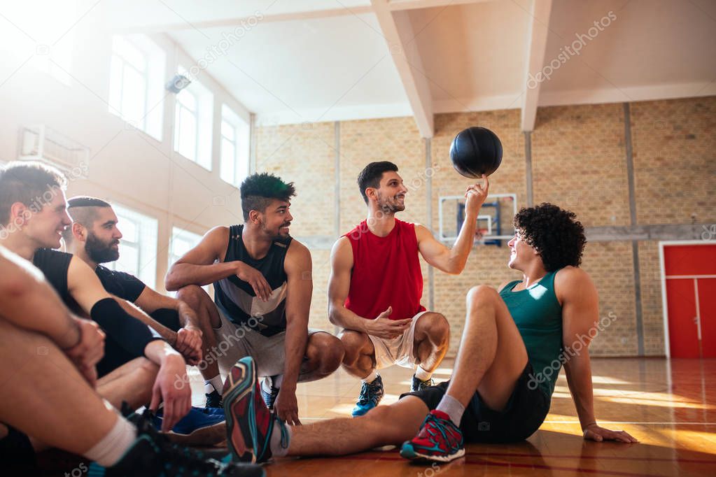Photo of basketball teammates sitting on the court and playing with the ball.