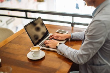 Kahve yudumlarken bir dizüstü bilgisayarda çalışan bir genç iş adamı fotoğrafı.