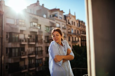 Bir Balkonda duran ve sabah güneşi zevk güzel kadın.