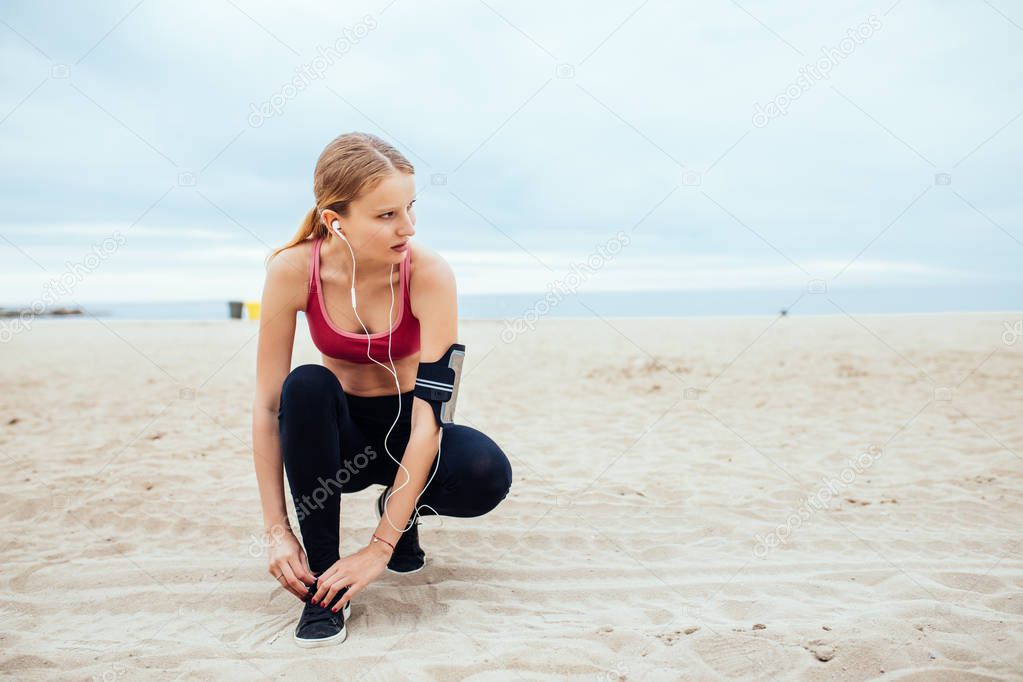 Handsome woman tying a shoe lace while running on the beach.