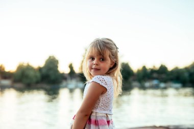 Nehir kenarında gülümseyen bir sarışın küçük kız portresi.