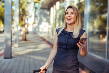 Cep telefonu kullaranarak ve takım elbise çantası çekerek çekici kadın.