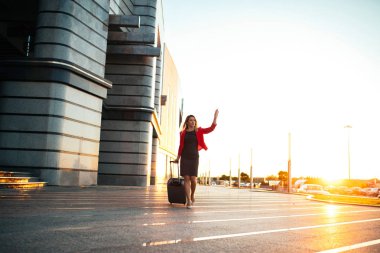 Bir bavul Havaalanı üzerinde çekerek ve sallayarak bir genç iş kadını tam uzunlukta portresi.
