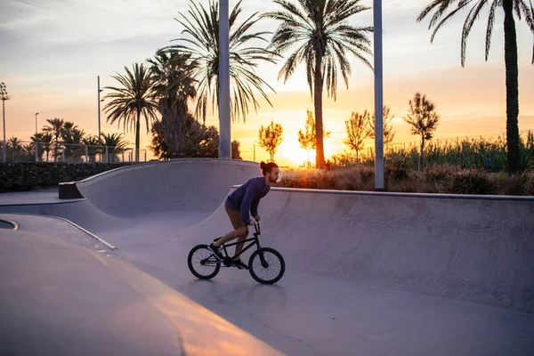 一名年轻男子在骑自行车的滑板公园在日落时分的镜头 — 图库照片