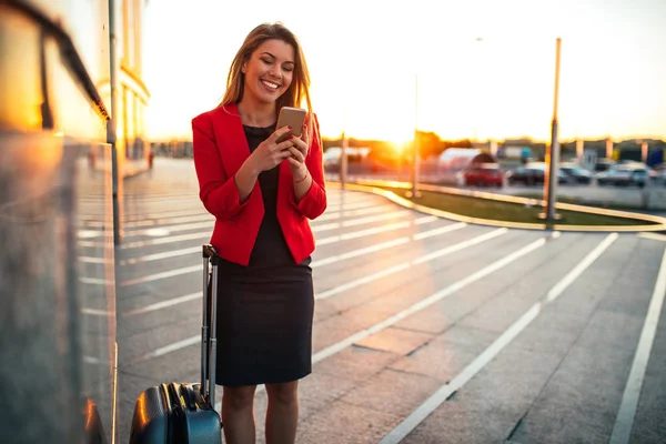 Portrait of a traveling business woman using mobile phone in the airport at sunset.