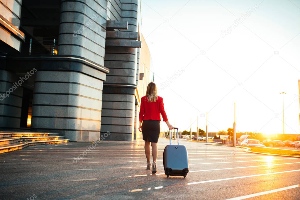 Portrait of a well dressed business woman pulling suitcase outdoors.