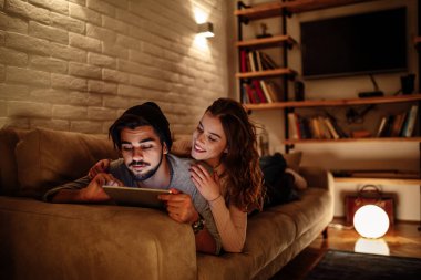 Kanepede yatan ve having fun dijital tablet üzerinde genç çiftin fotoğrafı.