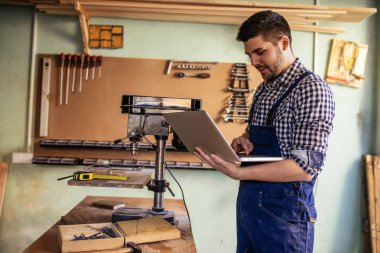 Genç bir marangoz atölyesinde dizüstü kullanarak portresi.