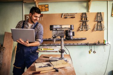 Portre çalışmaları sırasında dizüstü bilgisayar kullanarak bir gülümseyen genç marangoz.