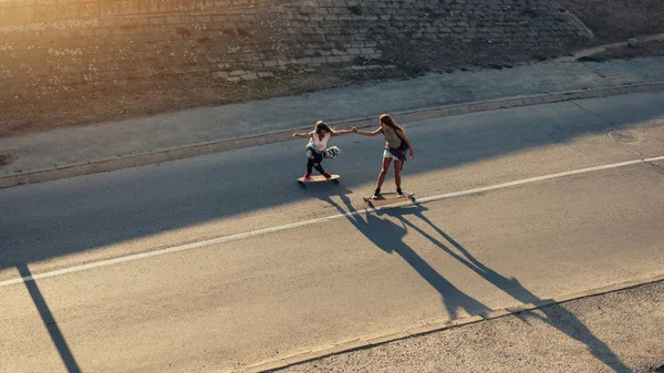 屋外の長いボードを運転している間手を繋いでいる二人の女の子 — ストック写真