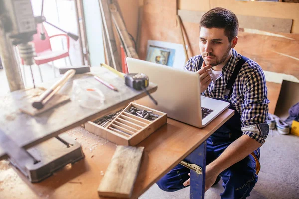 Masada oturan ve dizüstü bilgisayar kullanarak bir genç marangoz portresi.