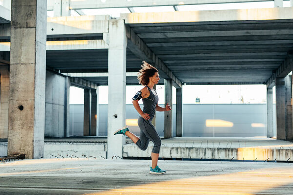 Full length portrait of an athlete woman running in full speed while listening to the music.