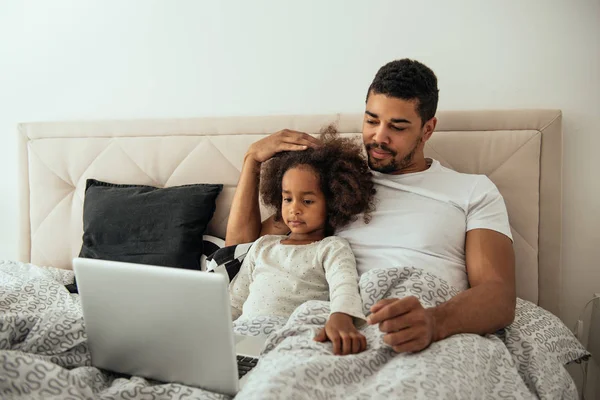 アフリカ系アメリカ人の父と娘のベッドで横になっていると ノート パソコンを使用しての肖像画 — ストック写真