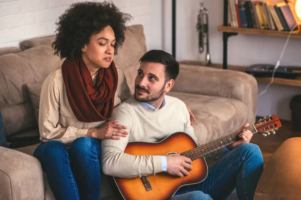 Young couple singing and playing guitar at home.