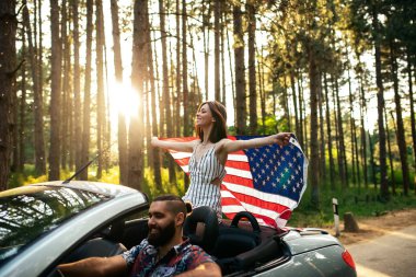 Genç bir çift bir Araba sürme keyfi bir kadeh. Bir Amerikan bayrağı tutan kadın odaklanmak.