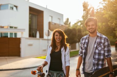 Gülümseyen genç bir çift açık havada longboards tutarken yürümeye portresi.