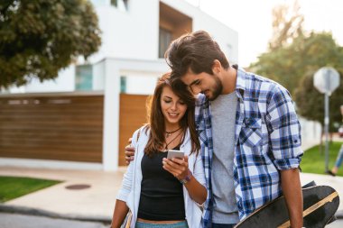 Cep telefonu açık havada ile eğlenceli ve longboards taşıyan genç bir çiftin fotoğrafı.