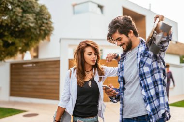 Genç bir çift mobil telefon kullanarak ve longboards açık havada tutan eğleniyor portresi.