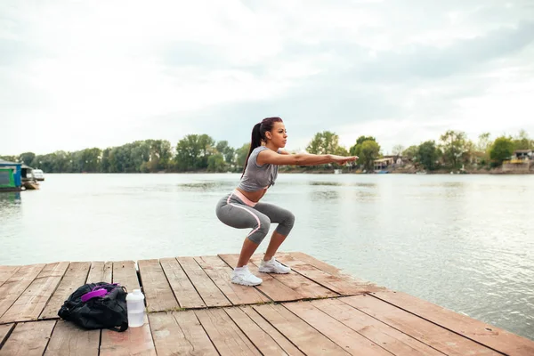 Portrait of an athlete woman doing squats outdoors by the lake.