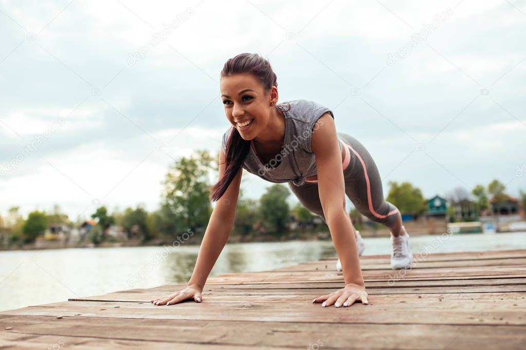 Full length portrait of a smiling athlete woman doing push ups on the deck.