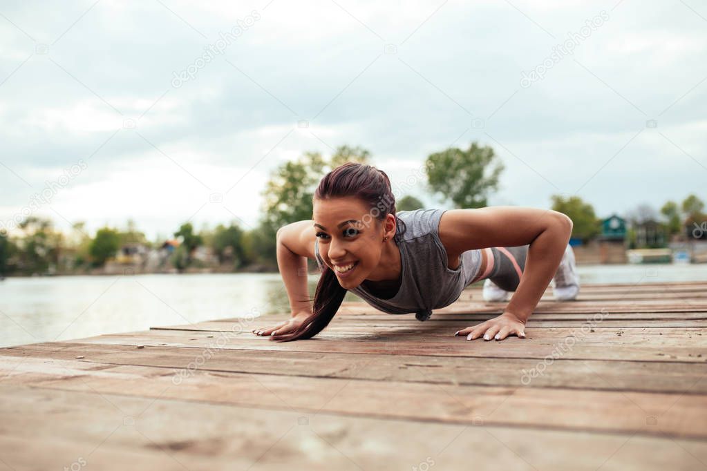 Satisfied young athlete woman doing push ups outdoors.