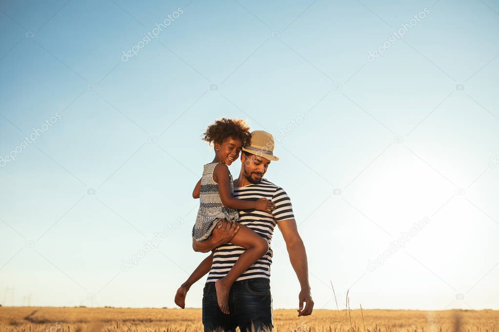 Portrait of an african american farmer carrying his daughter through wheat field.