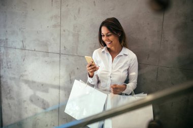 Cep telefonu kullaranarak ve poşetler içinde belgili tanımlık stok tutan güzel bir genç kadın portresi.