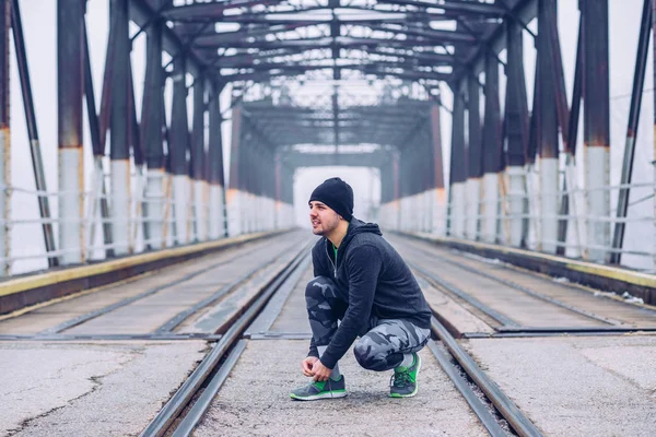 一张年轻运动男子在桥上系鞋带的照片 — 图库照片