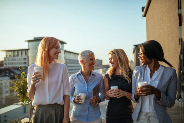 Portrait of four business women discussing about the next project with coffee on the rooftop.