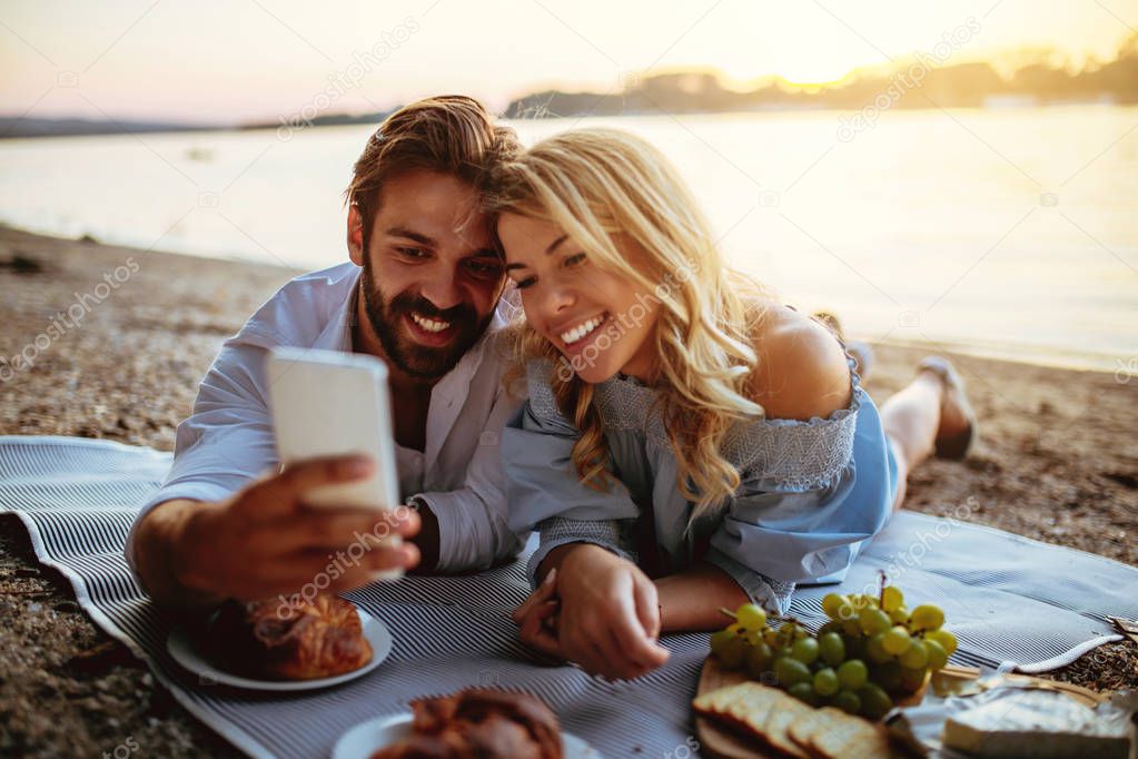 Young couple taking a photo with mobile phone on a picnic date.