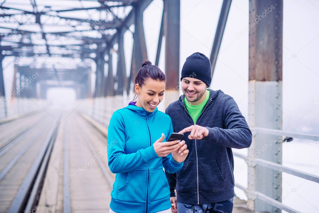 Portrait of a smiling young athlete couple having fun using mobile phone outdoors.