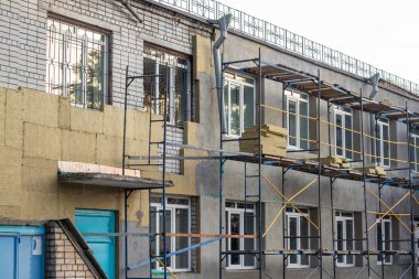 İskelelerle çevrili beyaz bir tuğla bina kahverengi yalıtım malzemeleriyle izole edilmiştir..