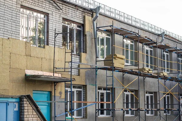 İskelelerle çevrili beyaz bir tuğla bina kahverengi yalıtım malzemeleriyle izole edilmiştir..