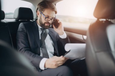 Takım elbiseli adam arabada cep telefonuyla konuşuyor.