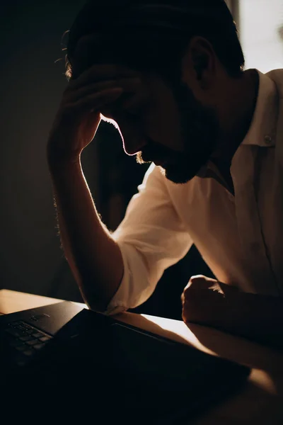 Cansado homem barbudo em silhueta trabalhando no laptop no escritório — Fotografia de Stock