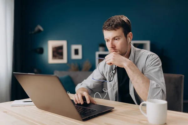 El hombre concentrado usando el ordenador portátil para el trabajo remoto en casa — Foto de Stock