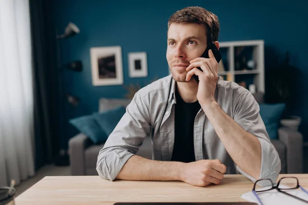 Masada otururken akıllı telefondan konuşan mutlu genç adam.
