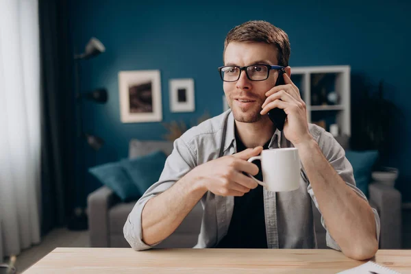Handsome guy talking on phone and drinking coffee at home