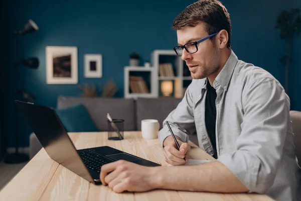 Hombre con gafas tomando notas mientras trabaja en el portátil — Foto de Stock