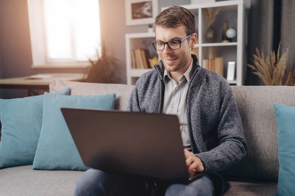 Sorrindo homem trabalhando no laptop enquanto sentado no sofá — Fotografia de Stock