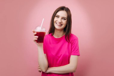 Pembe tişörtlü neşeli kız elinde soğuk taze kokteyl tutuyor.