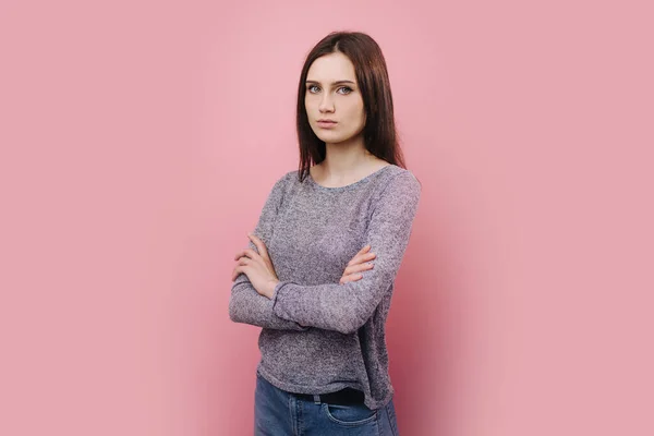 Pembe arka planda kolları çapraz duran ciddi bir kız.