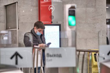 Rusya Haziran 2020. Moskova metrosu. Tıbbi maskeli bir adam turnikenin arkasında duruyor ve telefona bakıyor, Rusya 'daki koronavirüs salgınına. Virüs bulaşma riski var. renk
