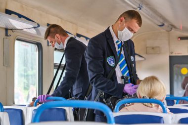 Moskova 2020 banliyö treni. Tıbbi maskeli bir erkek kontrolör yolcuların seyahat biletlerini kontrol ediyor. Rusya renginde pandemik korona virüsü