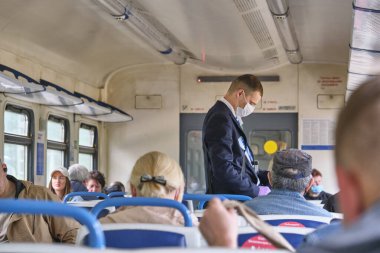 Moskova 2020 banliyö treni. Tıbbi maskeli bir erkek kontrolör yolcuların seyahat biletlerini kontrol ediyor. Rusya renginde pandemik korona virüsü