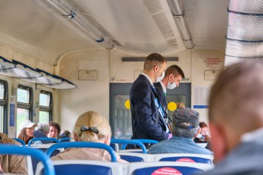 Moskova 2020 banliyö treni. Tıbbi maskeli bir erkek kontrolör yolcuların seyahat biletlerini kontrol ediyor. Rusya renginde pandemik korona virüsü
