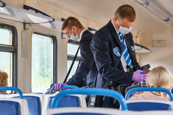 Moskova 2020 banliyö treni. Tıbbi maskeli bir erkek kontrolör yolcuların seyahat biletlerini kontrol ediyor. Rusya renginde pandemik korona virüsü