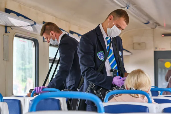 Moskova 2020 banliyö treni. Tıbbi maskeli bir erkek kontrolör yolcuların seyahat biletlerini kontrol ediyor. Rusya renginde pandemik korona virüsü