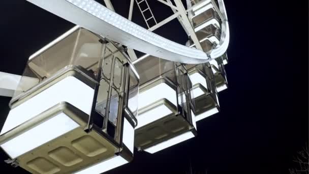 View of the Ferris wheel close up of white cabs that glow brightly at night. Concept: attractions - innocent and pleasant tourist leisure — Stock Video